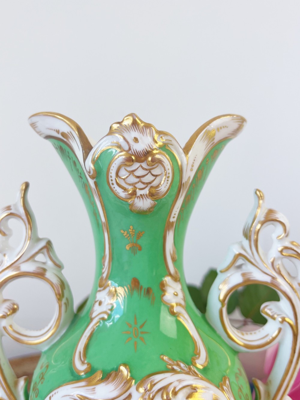 An apple green Rococo Revival porcelain vase featuring ornate gilded scroll handles, a quad-lobed pedestal base, and a central handpainted floral medallion on a white background. View IV