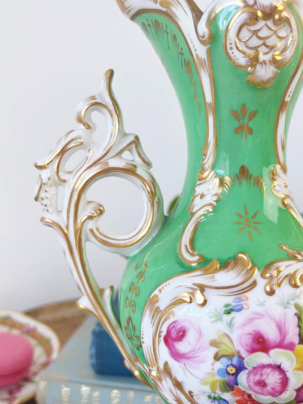 An apple green Rococo Revival porcelain vase featuring ornate gilded scroll handles, a quad-lobed pedestal base, and a central handpainted floral medallion on a white background. View V