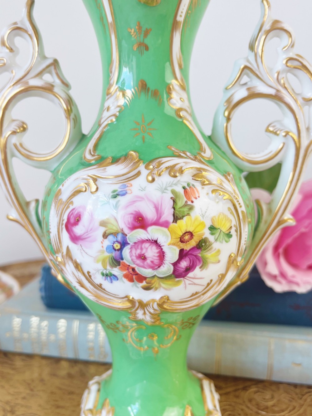An apple green Rococo Revival porcelain vase featuring ornate gilded scroll handles, a quad-lobed pedestal base, and a central handpainted floral medallion on a white background. View VI