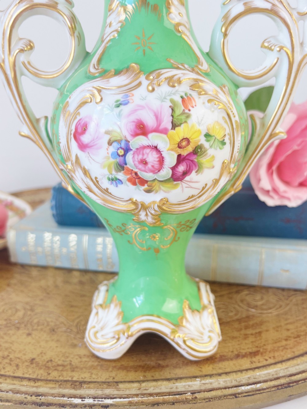 An apple green Rococo Revival porcelain vase featuring ornate gilded scroll handles, a quad-lobed pedestal base, and a central handpainted floral medallion on a white background. View VII
