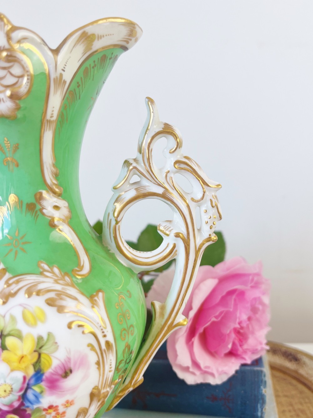 An apple green Rococo Revival porcelain vase featuring ornate gilded scroll handles, a quad-lobed pedestal base, and a central handpainted floral medallion on a white background. View IX