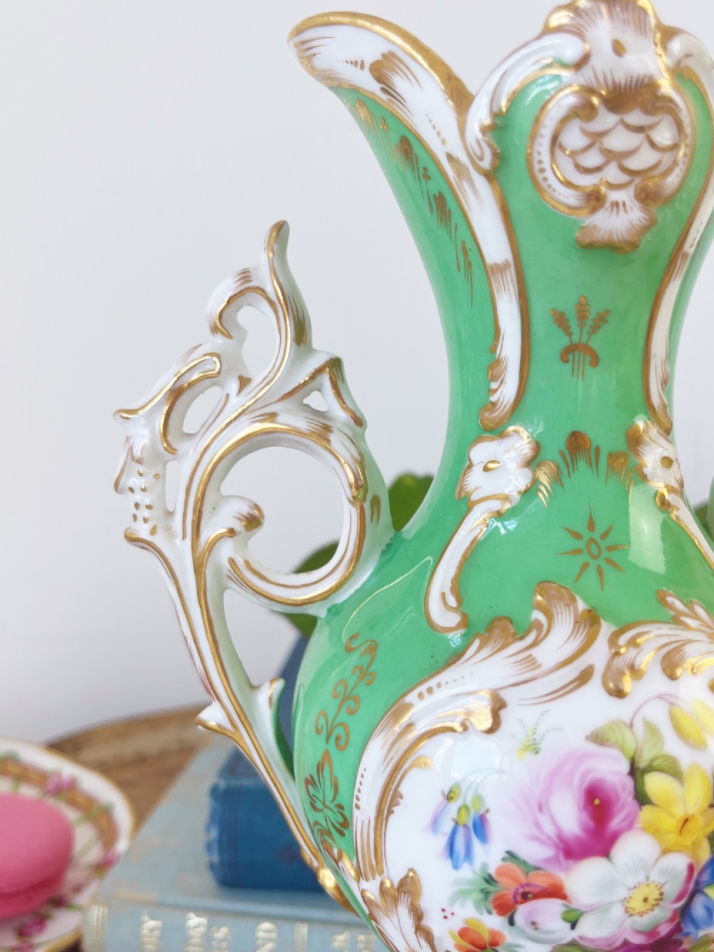 An apple green Rococo Revival porcelain vase featuring ornate gilded scroll handles, a quad-lobed pedestal base, and a central handpainted floral medallion on a white background. View X