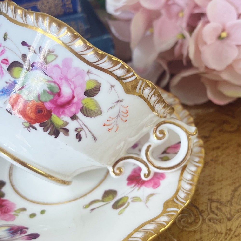 A white porcelain teacup and saucer set featuring hand-painted floral motifs, a gadrooned rim, and gilded scroll accents. View II