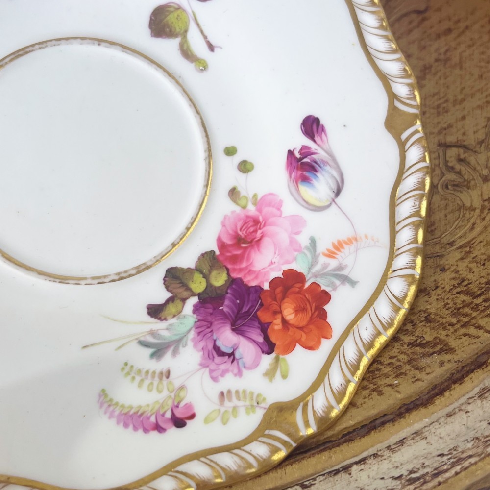A white porcelain teacup and saucer set featuring hand-painted floral motifs, a gadrooned rim, and gilded scroll accents. View VI