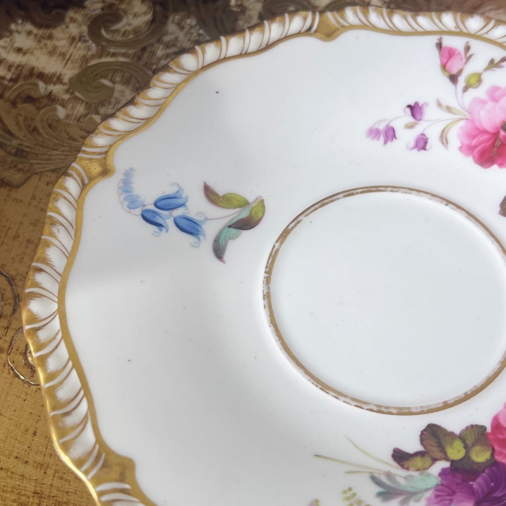 A white porcelain teacup and saucer set featuring hand-painted floral motifs, a gadrooned rim, and gilded scroll accents. View VIII
