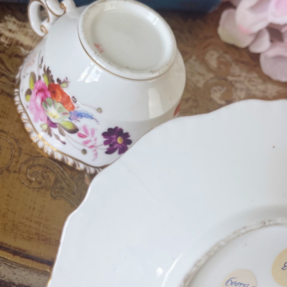 A white porcelain teacup and saucer set featuring hand-painted floral motifs, a gadrooned rim, and gilded scroll accents. View IX