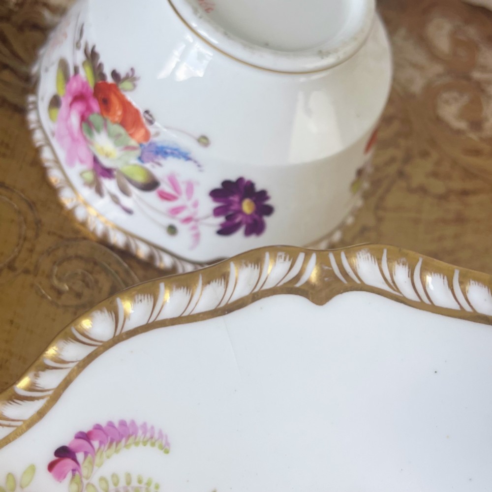 A white porcelain teacup and saucer set featuring hand-painted floral motifs, a gadrooned rim, and gilded scroll accents. View X