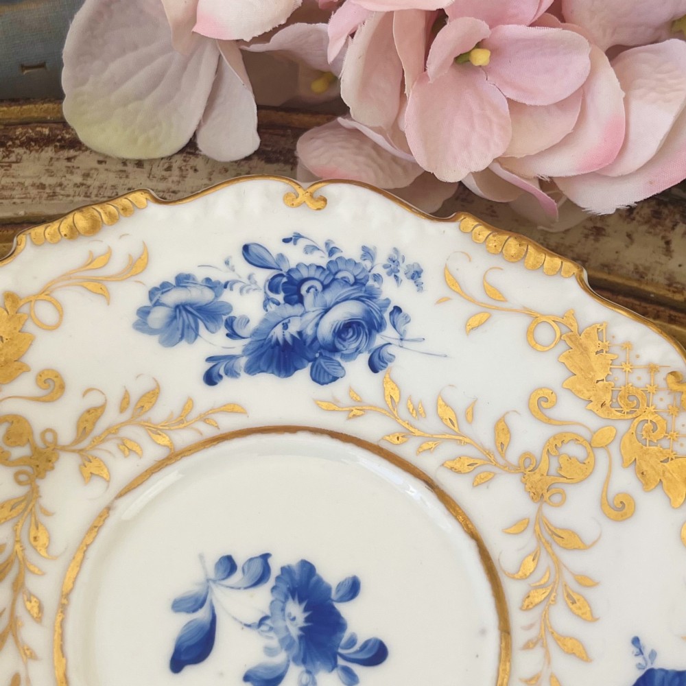 An antique Regency period white porcelain teacup and saucer featuring hand-painted blue floral motifs and gilded ornate rim embellishments. View XIV