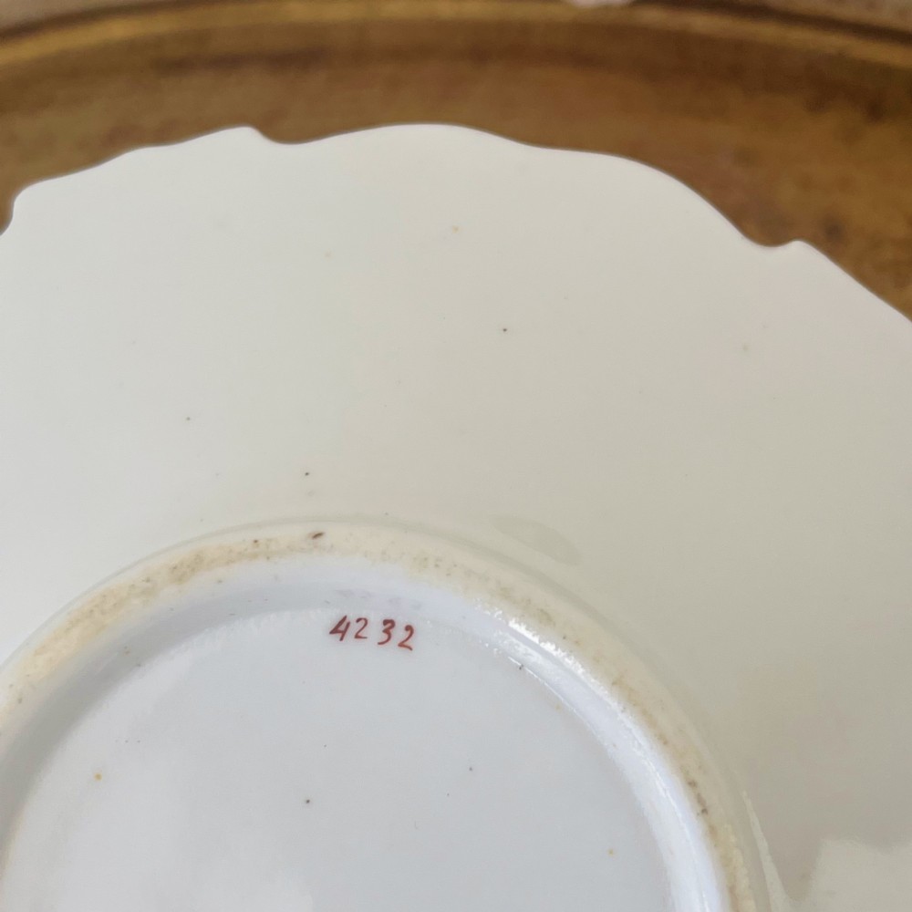 An antique Regency period white porcelain teacup and saucer featuring hand-painted blue floral motifs and gilded ornate rim embellishments. View XV