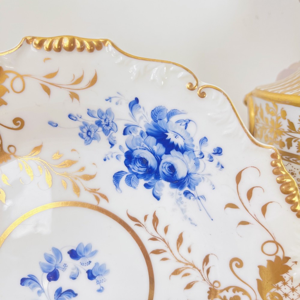 An early nineteenth-century white porcelain plate featuring hand-painted blue floral clusters, ornate gilded foliage along the scalloped rim, and a central circular gilt border. View II