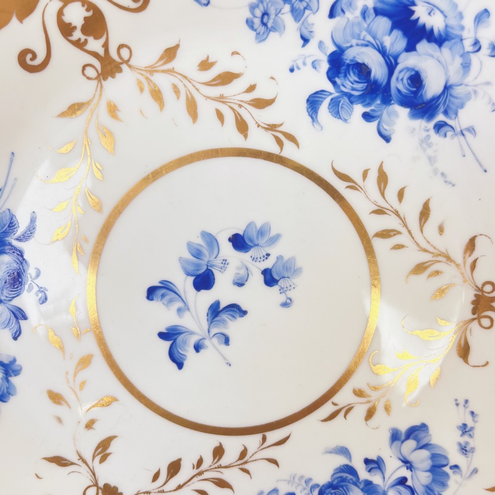 An early nineteenth-century white porcelain plate featuring hand-painted blue floral clusters, ornate gilded foliage along the scalloped rim, and a central circular gilt border. View VIII