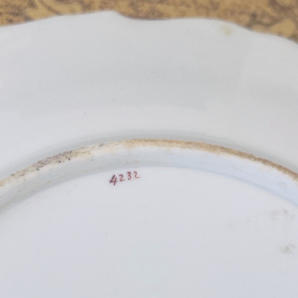 An early nineteenth-century white porcelain plate featuring hand-painted blue floral clusters, ornate gilded foliage along the scalloped rim, and a central circular gilt border. View IX