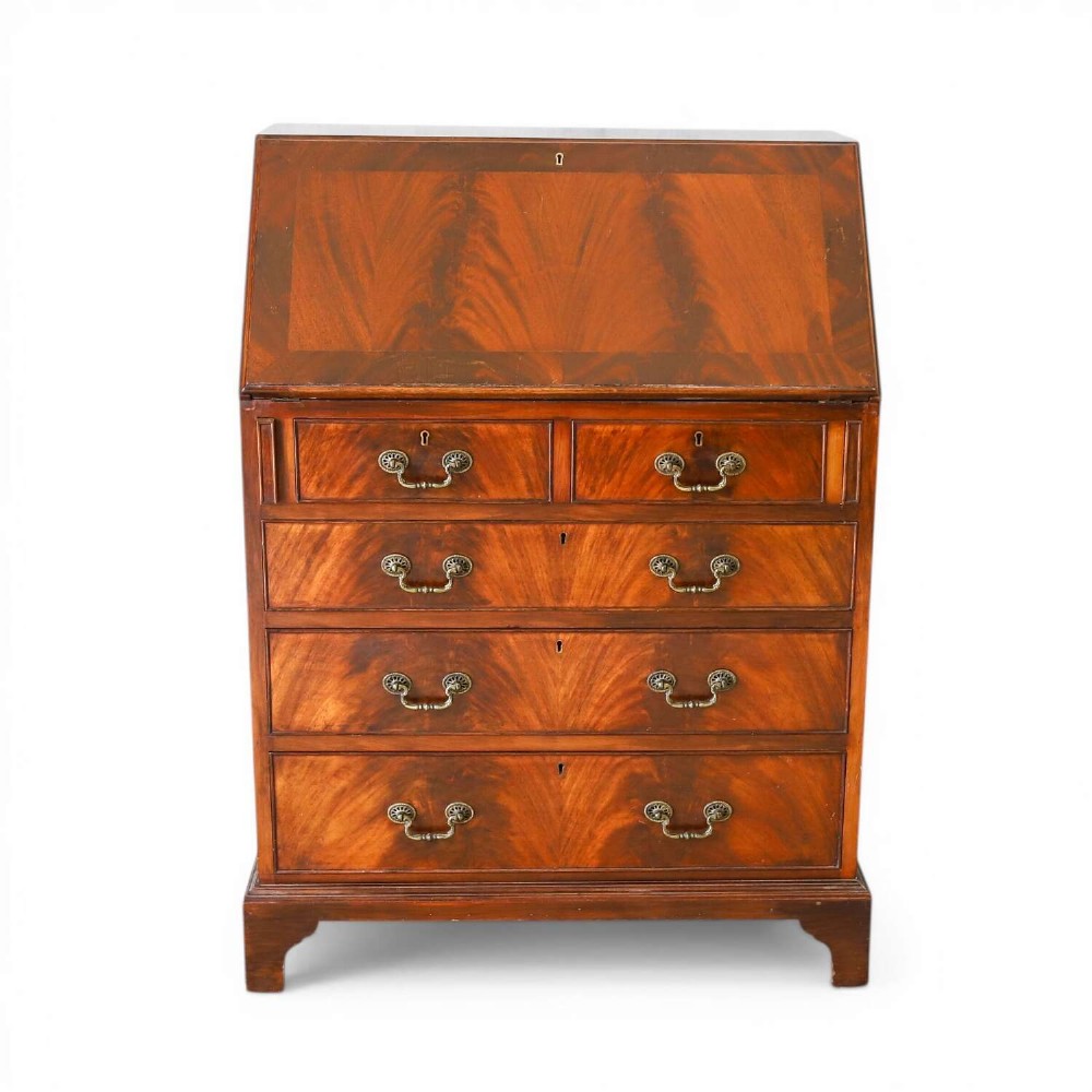 An English 1930s flame mahogany slant-front writing bureau featuring four lower drawers and brass handles.