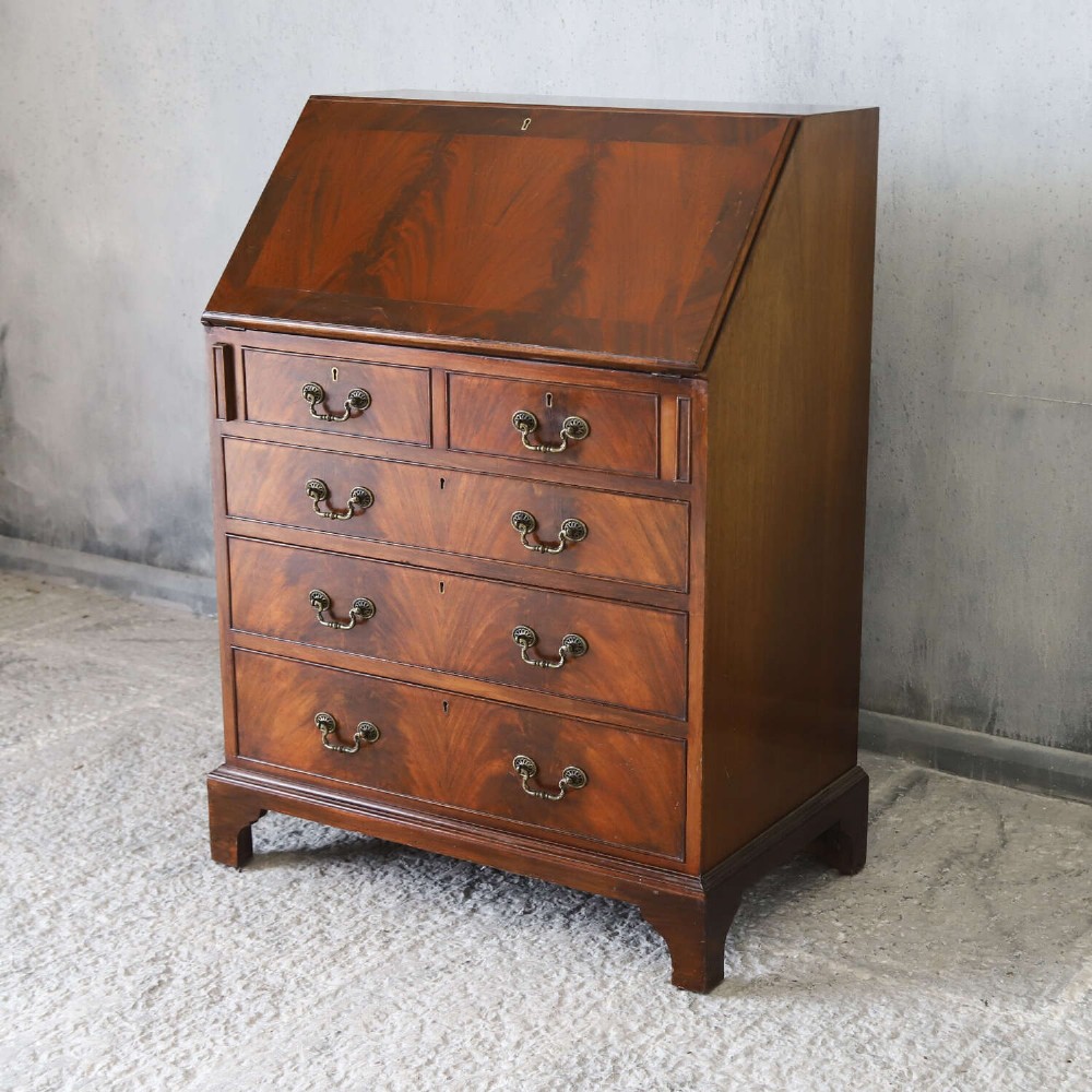 An English 1930s flame mahogany slant-front writing bureau featuring four lower drawers and brass handles. View II