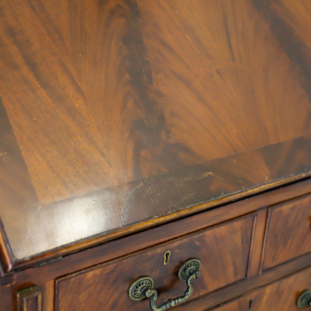 An English 1930s flame mahogany slant-front writing bureau featuring four lower drawers and brass handles. View VIII