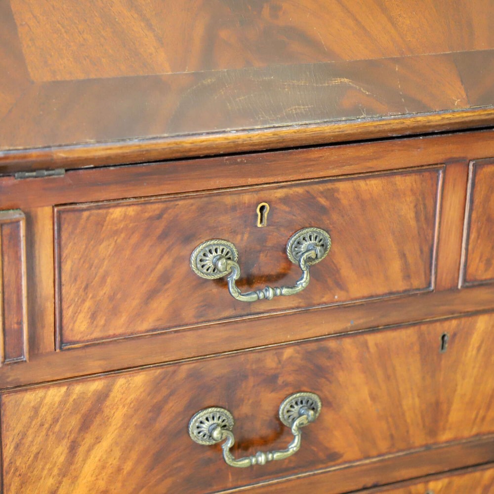 An English 1930s flame mahogany slant-front writing bureau featuring four lower drawers and brass handles. View X