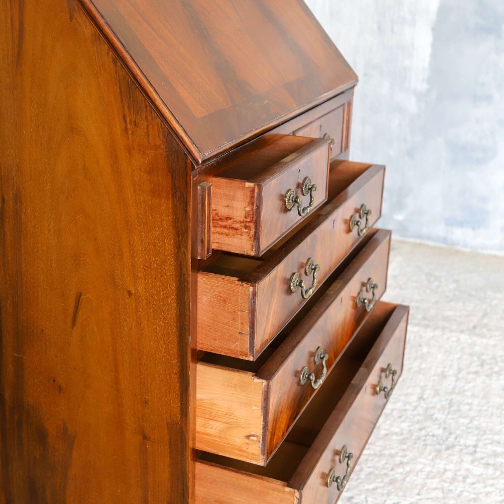 An English 1930s flame mahogany slant-front writing bureau featuring four lower drawers and brass handles. View XI