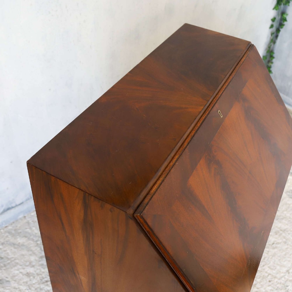 An English 1930s flame mahogany slant-front writing bureau featuring four lower drawers and brass handles. View XIII