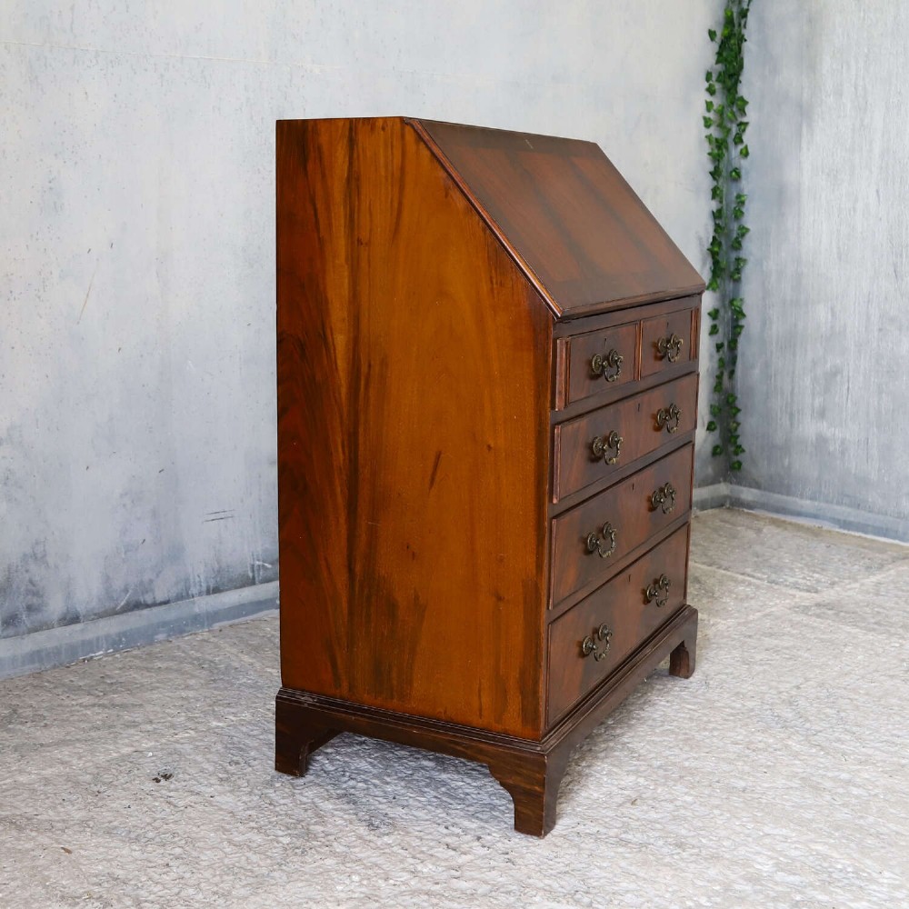 An English 1930s flame mahogany slant-front writing bureau featuring four lower drawers and brass handles. View XIV