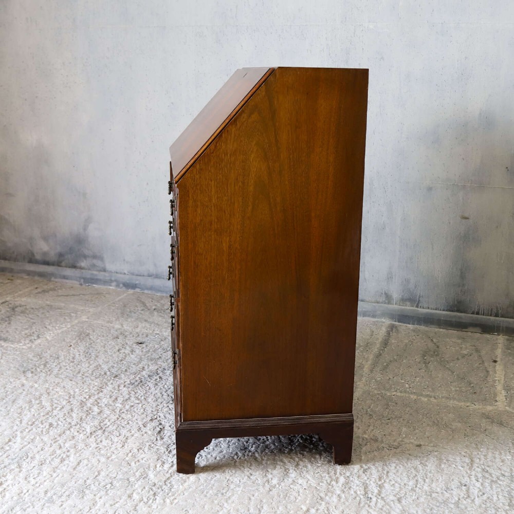 An English 1930s flame mahogany slant-front writing bureau featuring four lower drawers and brass handles. View XV
