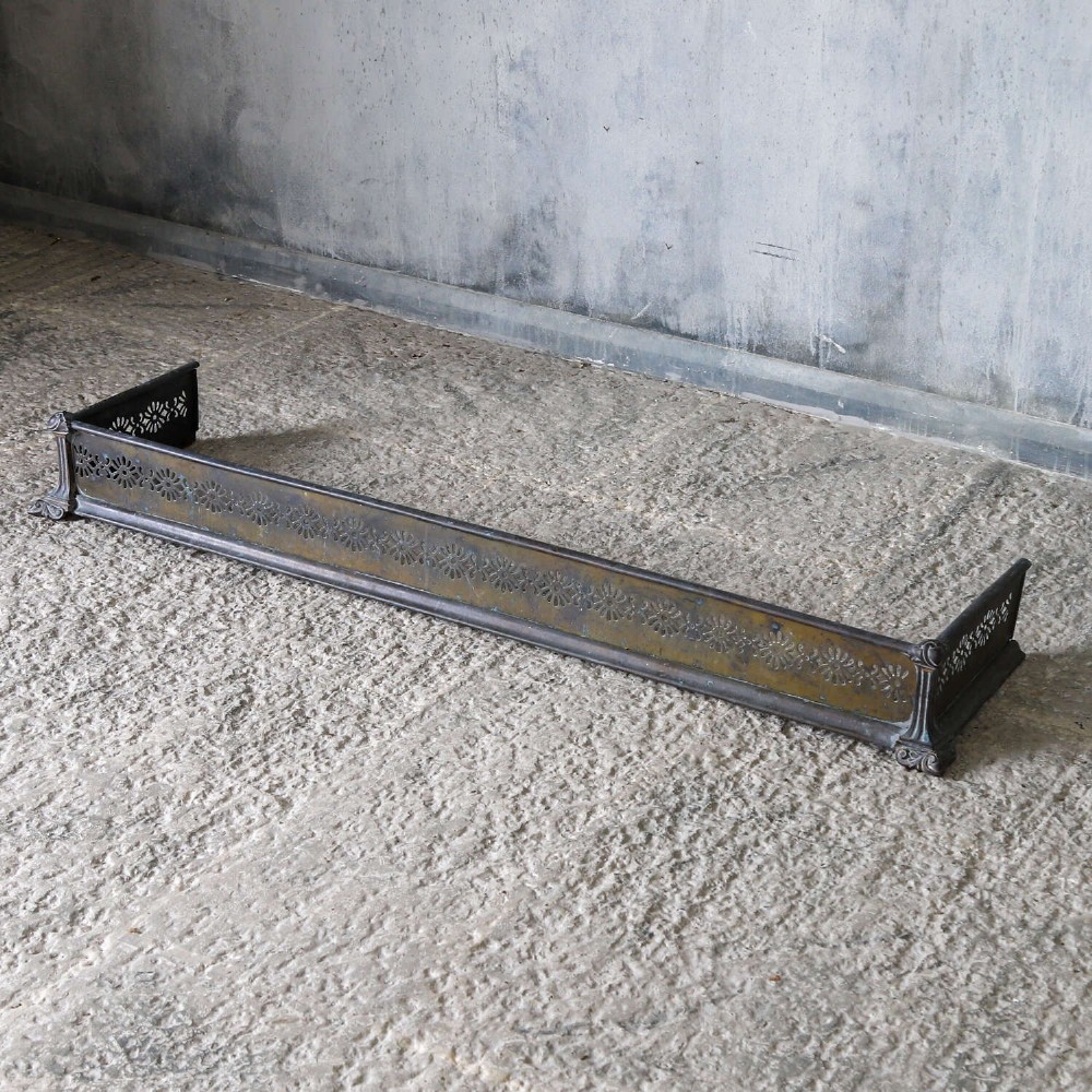 An English Art Nouveau fireplace fender constructed from brass and steel featuring a continuous pierced daisy motif. View II