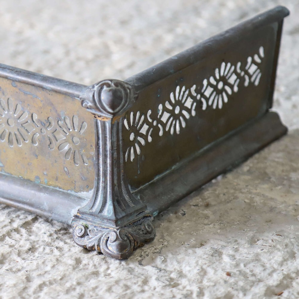 An English Art Nouveau fireplace fender constructed from brass and steel featuring a continuous pierced daisy motif. View III