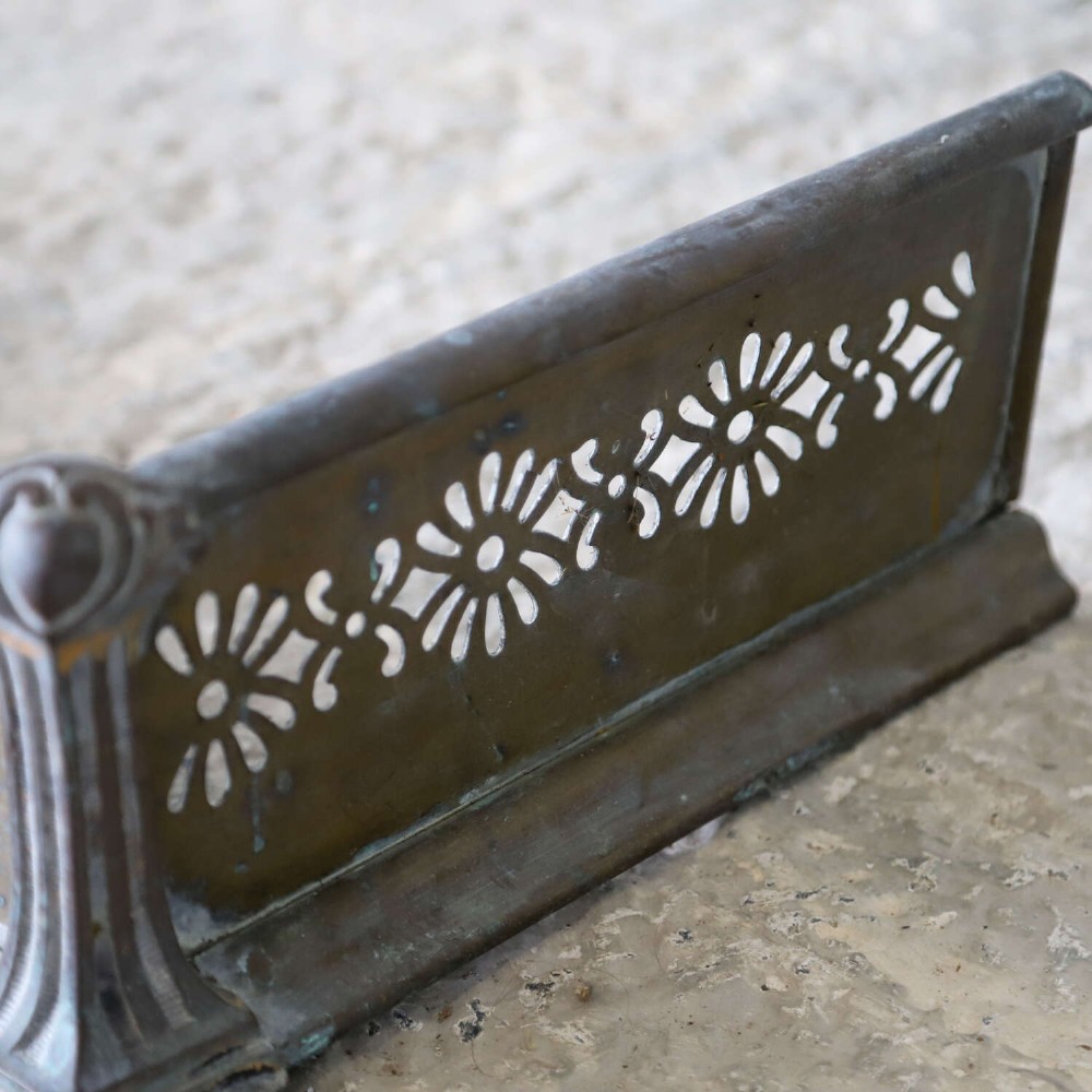 An English Art Nouveau fireplace fender constructed from brass and steel featuring a continuous pierced daisy motif. View IV