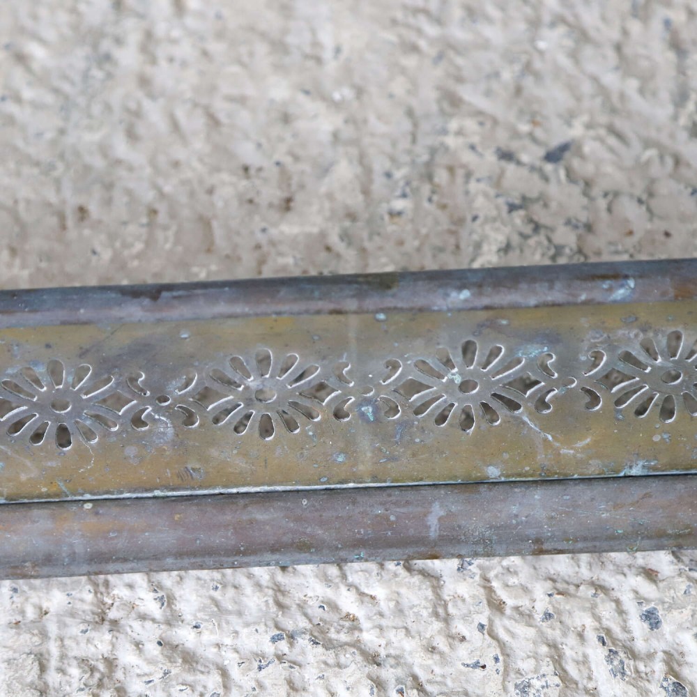 An English Art Nouveau fireplace fender constructed from brass and steel featuring a continuous pierced daisy motif. View VI