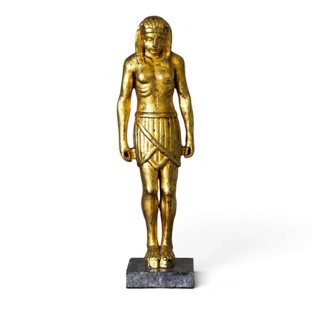 A 19th-century Egyptian Revival gilt wooden standing figure mounted on a dark square stone base.