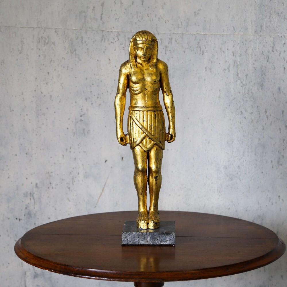 A 19th-century Egyptian Revival gilt wooden standing figure mounted on a dark square stone base. View II