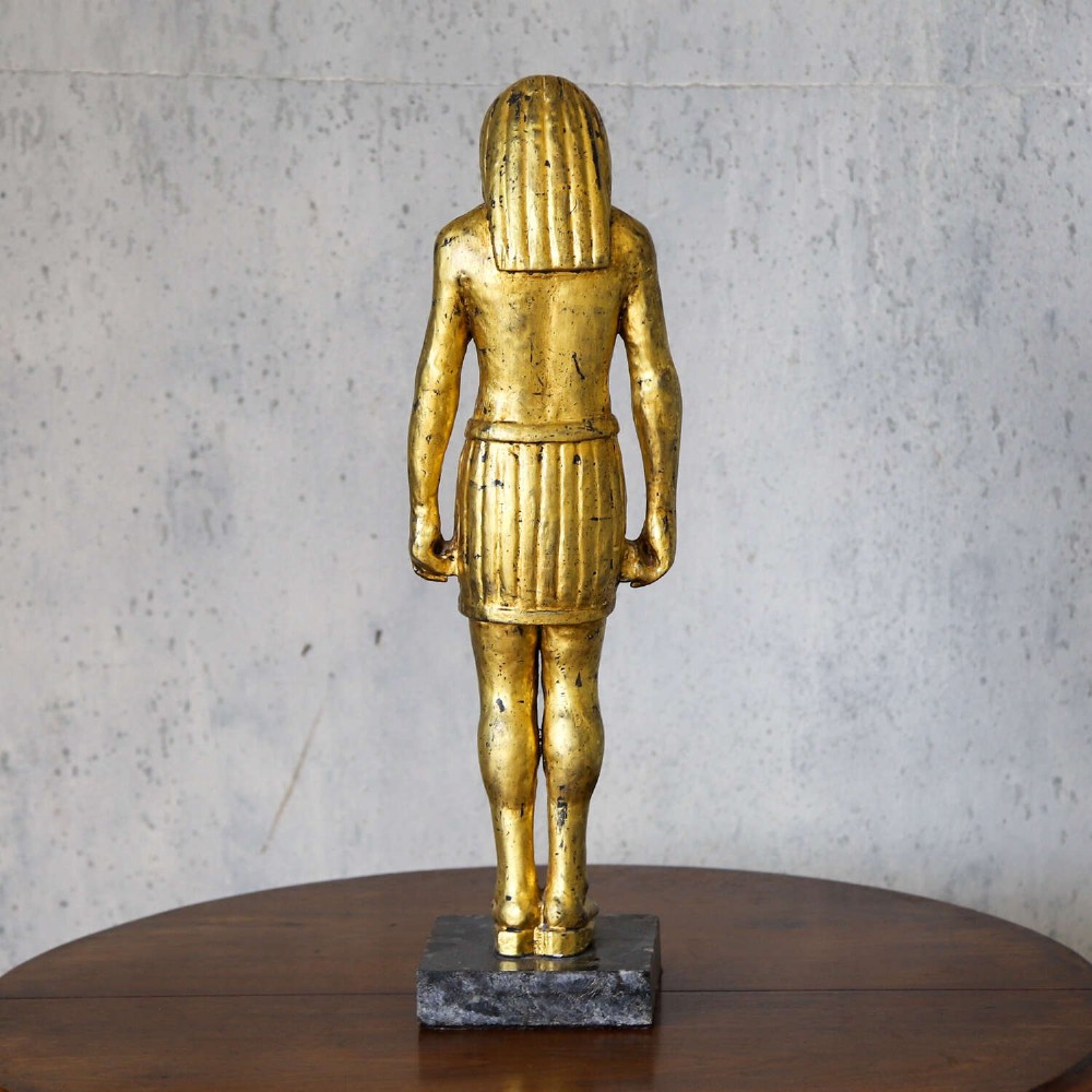 A 19th-century Egyptian Revival gilt wooden standing figure mounted on a dark square stone base. View VII