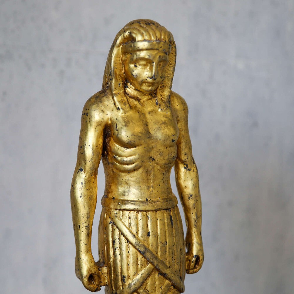 A 19th-century Egyptian Revival gilt wooden standing figure mounted on a dark square stone base. View X