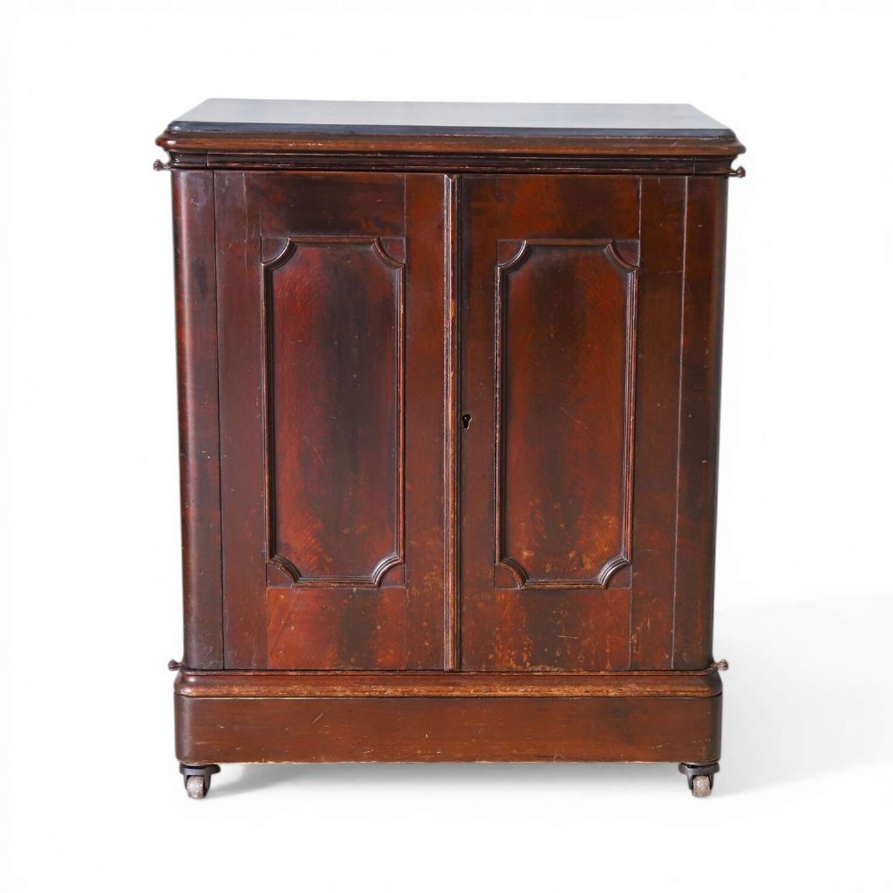 A late 19th-century dark mahogany office cupboard featuring two recessed panel doors, central brass keyhole escutcheon, plinth base, and fitted metal castors.