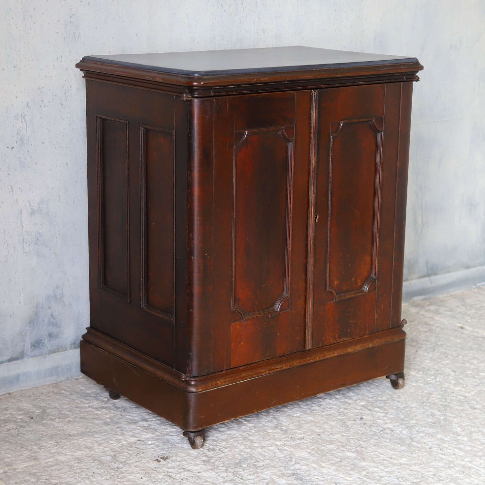 A late 19th-century dark mahogany office cupboard featuring two recessed panel doors, central brass keyhole escutcheon, plinth base, and fitted metal castors. View II