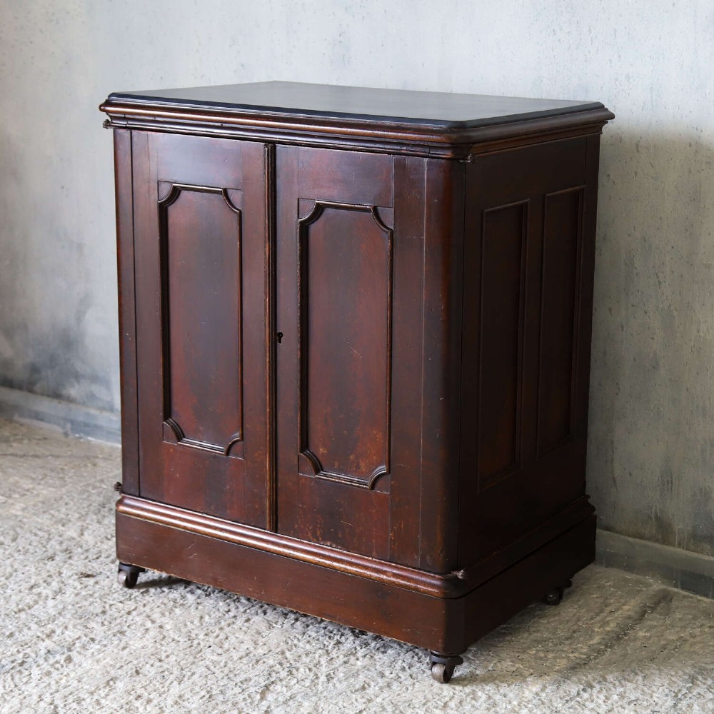 A late 19th-century dark mahogany office cupboard featuring two recessed panel doors, central brass keyhole escutcheon, plinth base, and fitted metal castors. View III