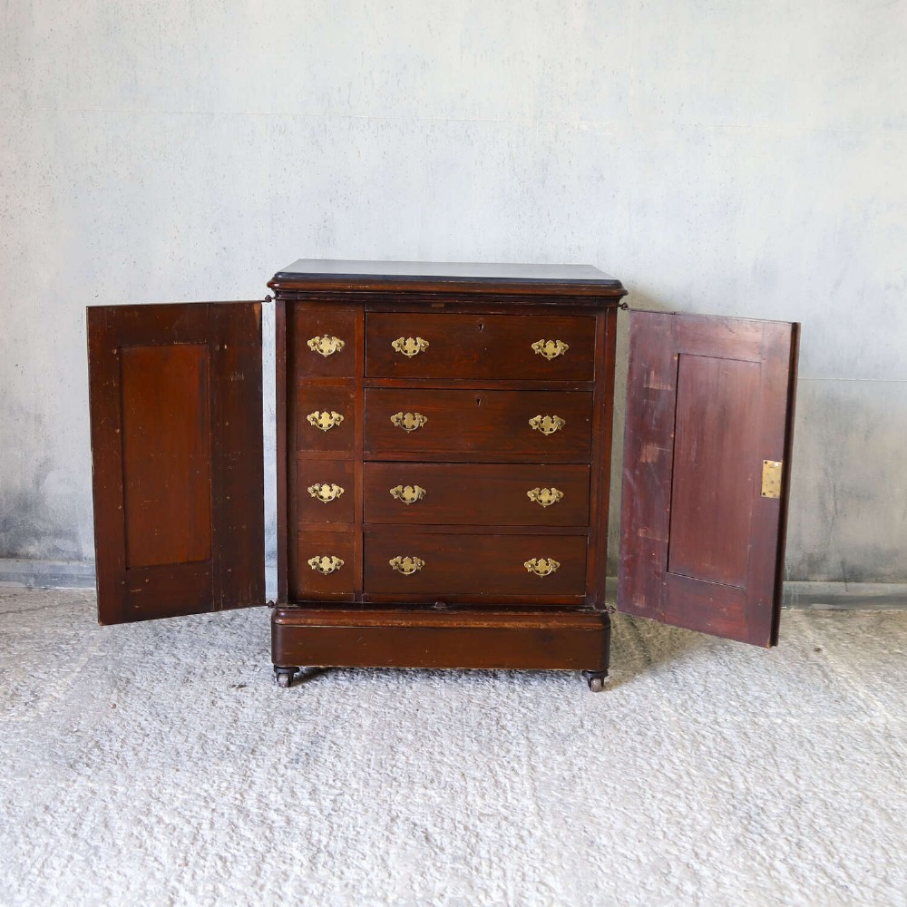 A late 19th-century dark mahogany office cupboard featuring two recessed panel doors, central brass keyhole escutcheon, plinth base, and fitted metal castors. View IV