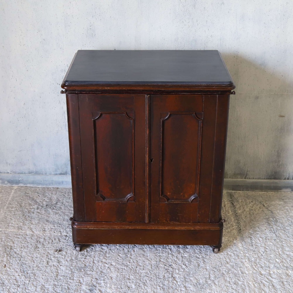 A late 19th-century dark mahogany office cupboard featuring two recessed panel doors, central brass keyhole escutcheon, plinth base, and fitted metal castors. View V