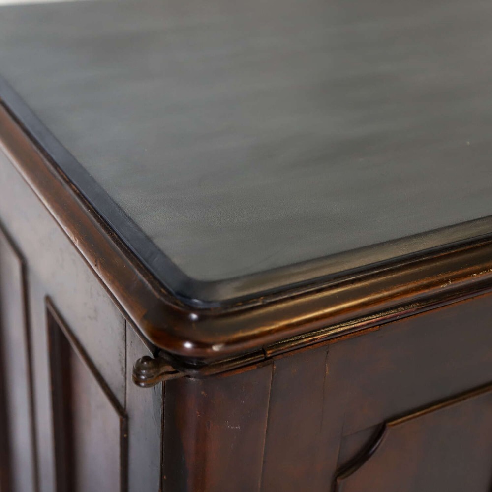 A late 19th-century dark mahogany office cupboard featuring two recessed panel doors, central brass keyhole escutcheon, plinth base, and fitted metal castors. View VI