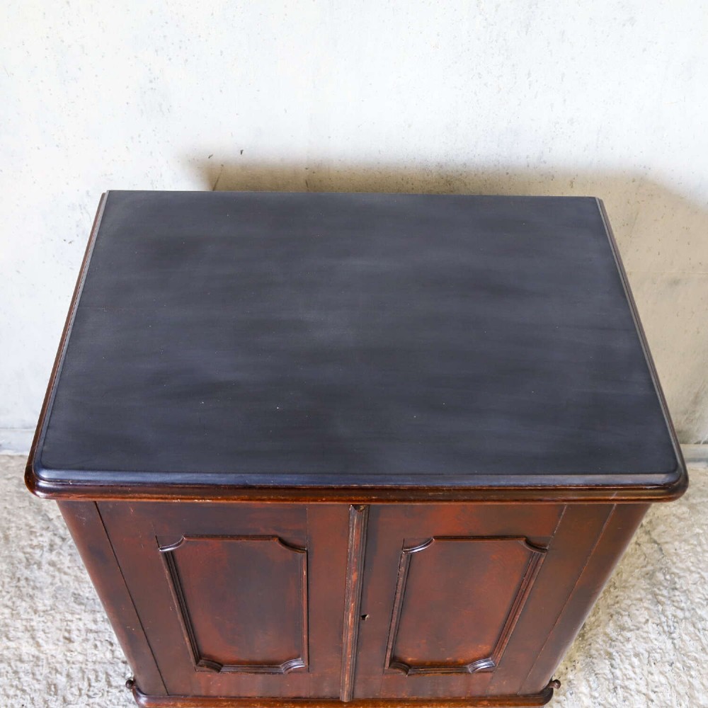 A late 19th-century dark mahogany office cupboard featuring two recessed panel doors, central brass keyhole escutcheon, plinth base, and fitted metal castors. View VII