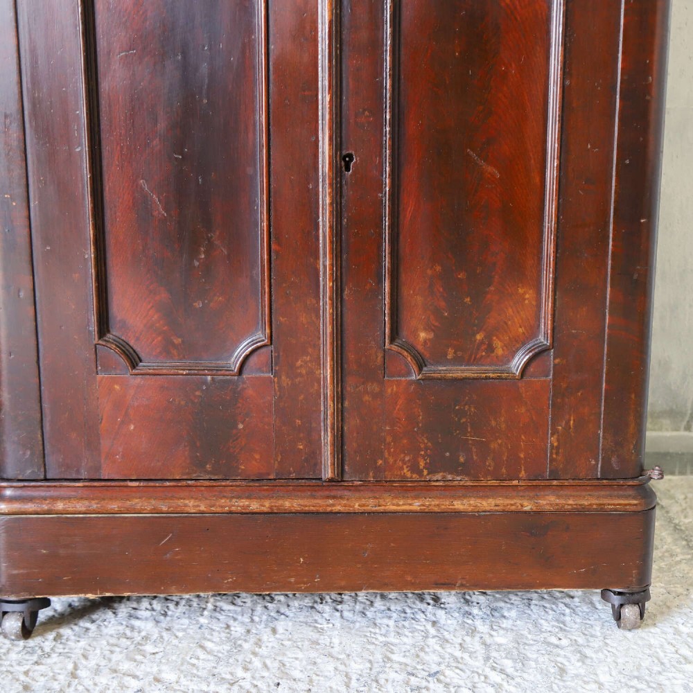 A late 19th-century dark mahogany office cupboard featuring two recessed panel doors, central brass keyhole escutcheon, plinth base, and fitted metal castors. View VIII