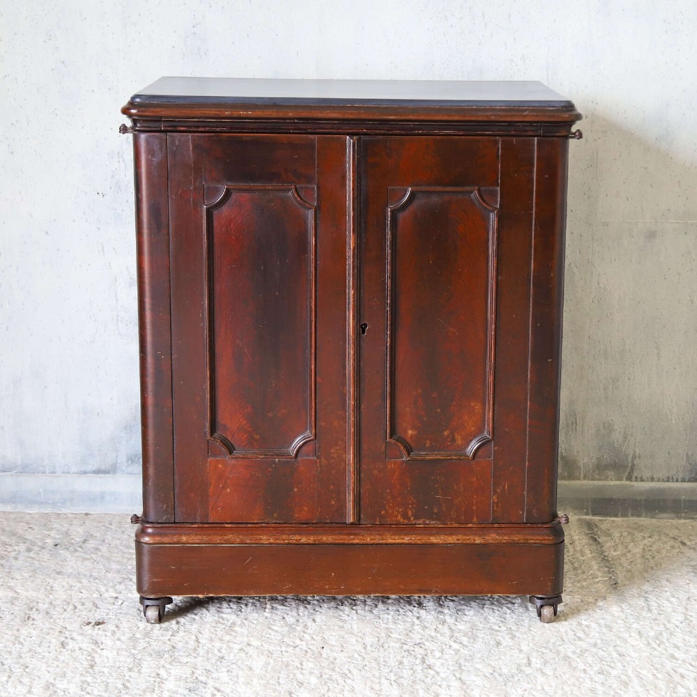 A late 19th-century dark mahogany office cupboard featuring two recessed panel doors, central brass keyhole escutcheon, plinth base, and fitted metal castors. View IX