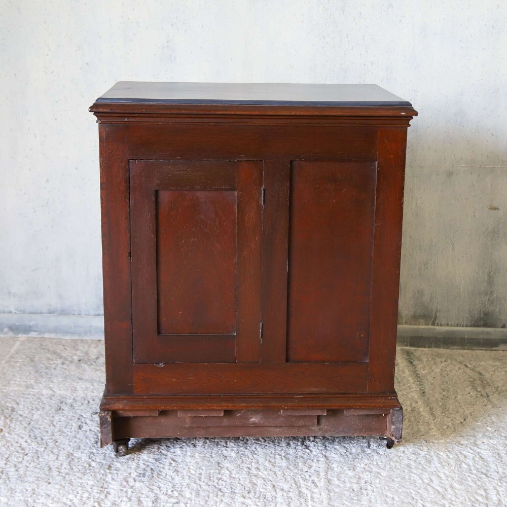 A late 19th-century dark mahogany office cupboard featuring two recessed panel doors, central brass keyhole escutcheon, plinth base, and fitted metal castors. View XI