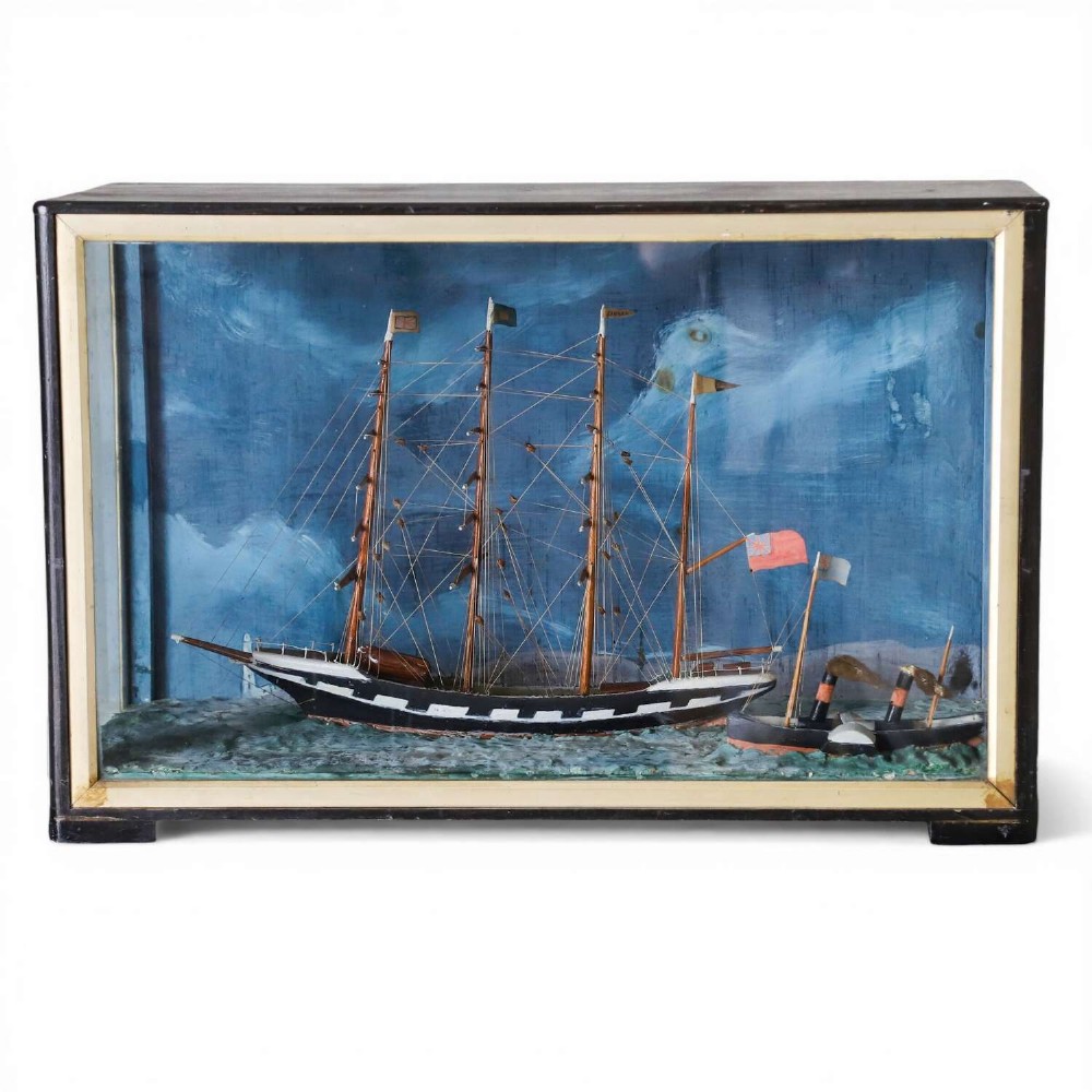A glazed wooden shadow box containing a three-dimensional diorama of a four-masted sailing ship and a steam barge against a painted blue background.