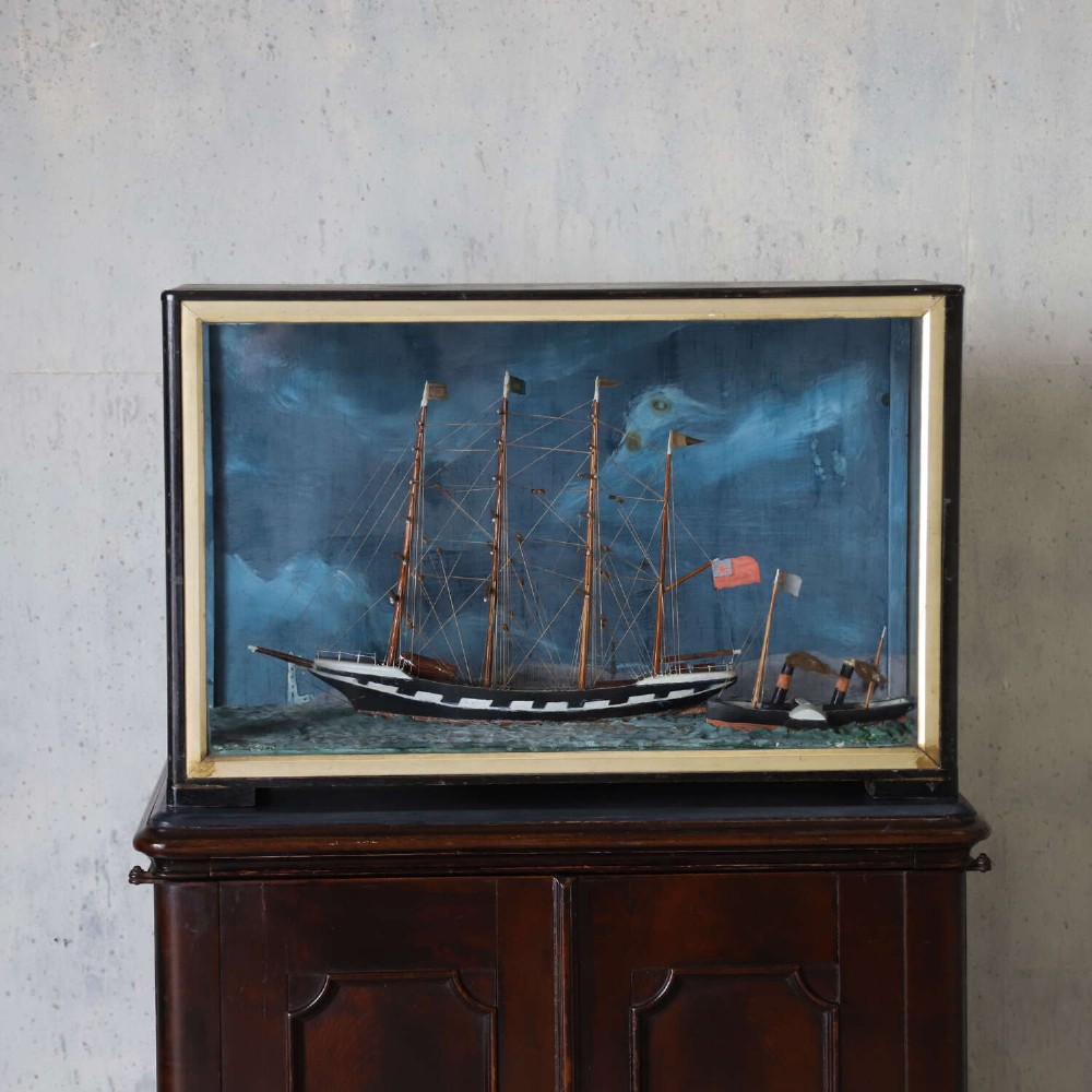 A glazed wooden shadow box containing a three-dimensional diorama of a four-masted sailing ship and a steam barge against a painted blue background. View II