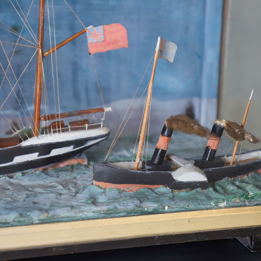 A glazed wooden shadow box containing a three-dimensional diorama of a four-masted sailing ship and a steam barge against a painted blue background. View III
