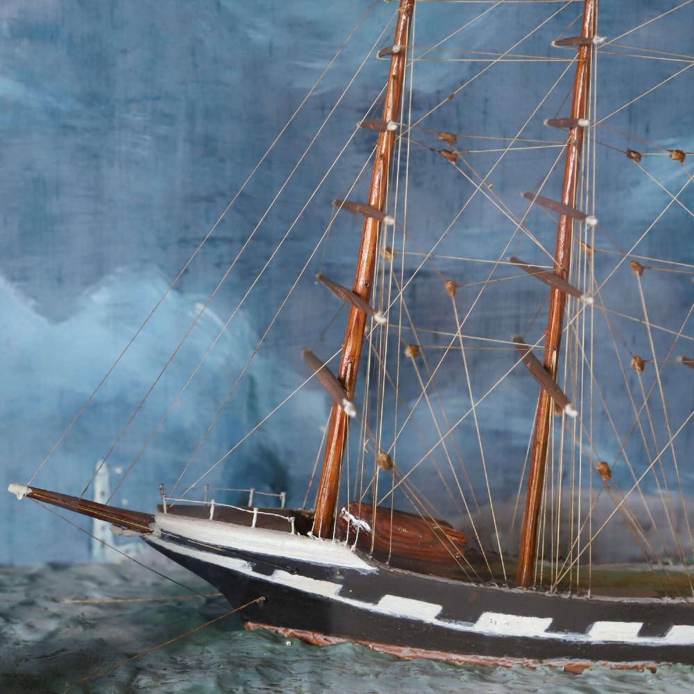 A glazed wooden shadow box containing a three-dimensional diorama of a four-masted sailing ship and a steam barge against a painted blue background. View V