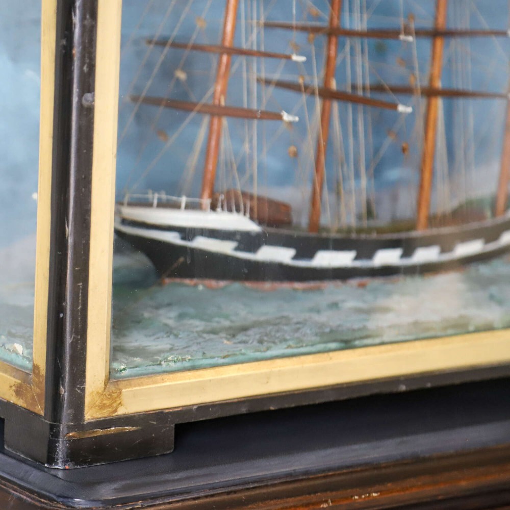 A glazed wooden shadow box containing a three-dimensional diorama of a four-masted sailing ship and a steam barge against a painted blue background. View VII
