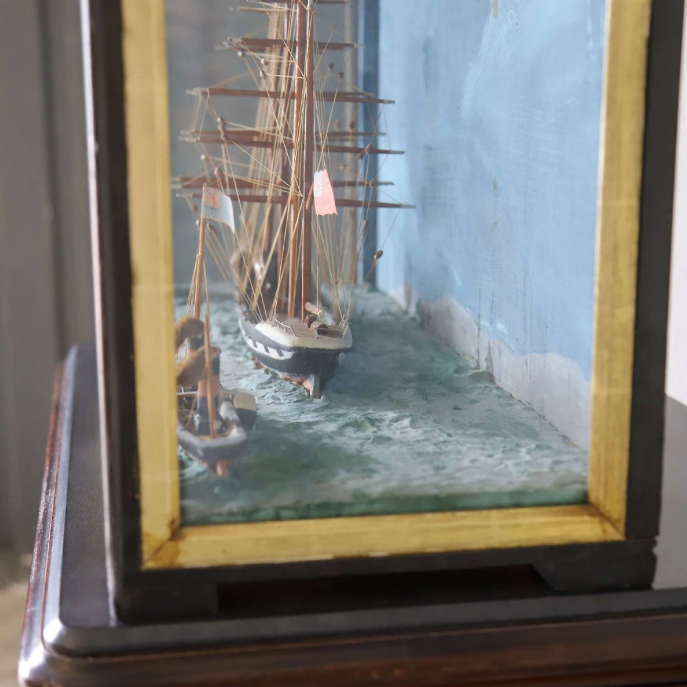 A glazed wooden shadow box containing a three-dimensional diorama of a four-masted sailing ship and a steam barge against a painted blue background. View IX
