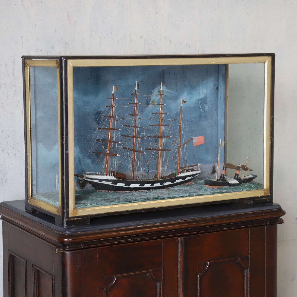 A glazed wooden shadow box containing a three-dimensional diorama of a four-masted sailing ship and a steam barge against a painted blue background. View X
