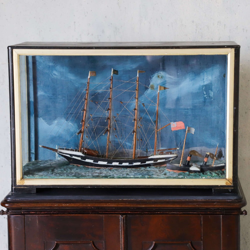 A glazed wooden shadow box containing a three-dimensional diorama of a four-masted sailing ship and a steam barge against a painted blue background. View XI